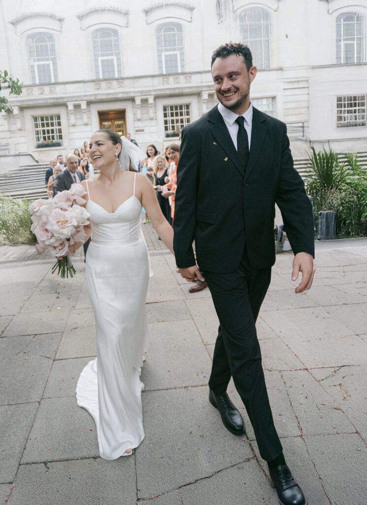 Couple walking out of Hackney Hall in full joy after wedding married. Photo by London Wedding Photographer, Pia Bacino