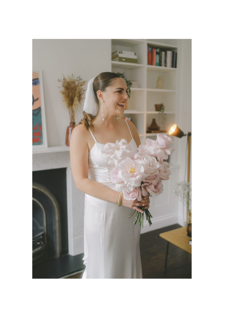 Bride's reaction to seeing her bridesmaids for the first time. Portrait of bride smiling holding her bouquet. Photo by London Wedding Photographer, Pia Bacino