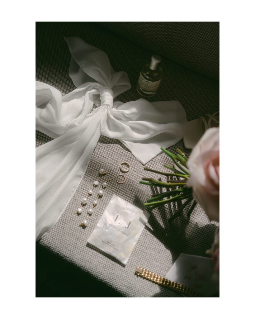 Bride's details on her wedding day. Seen are her pearl earrings, wedding rings, her bouquet, her perfume and her bridal bow. Photo by London Wedding Photographer, Pia Bacino