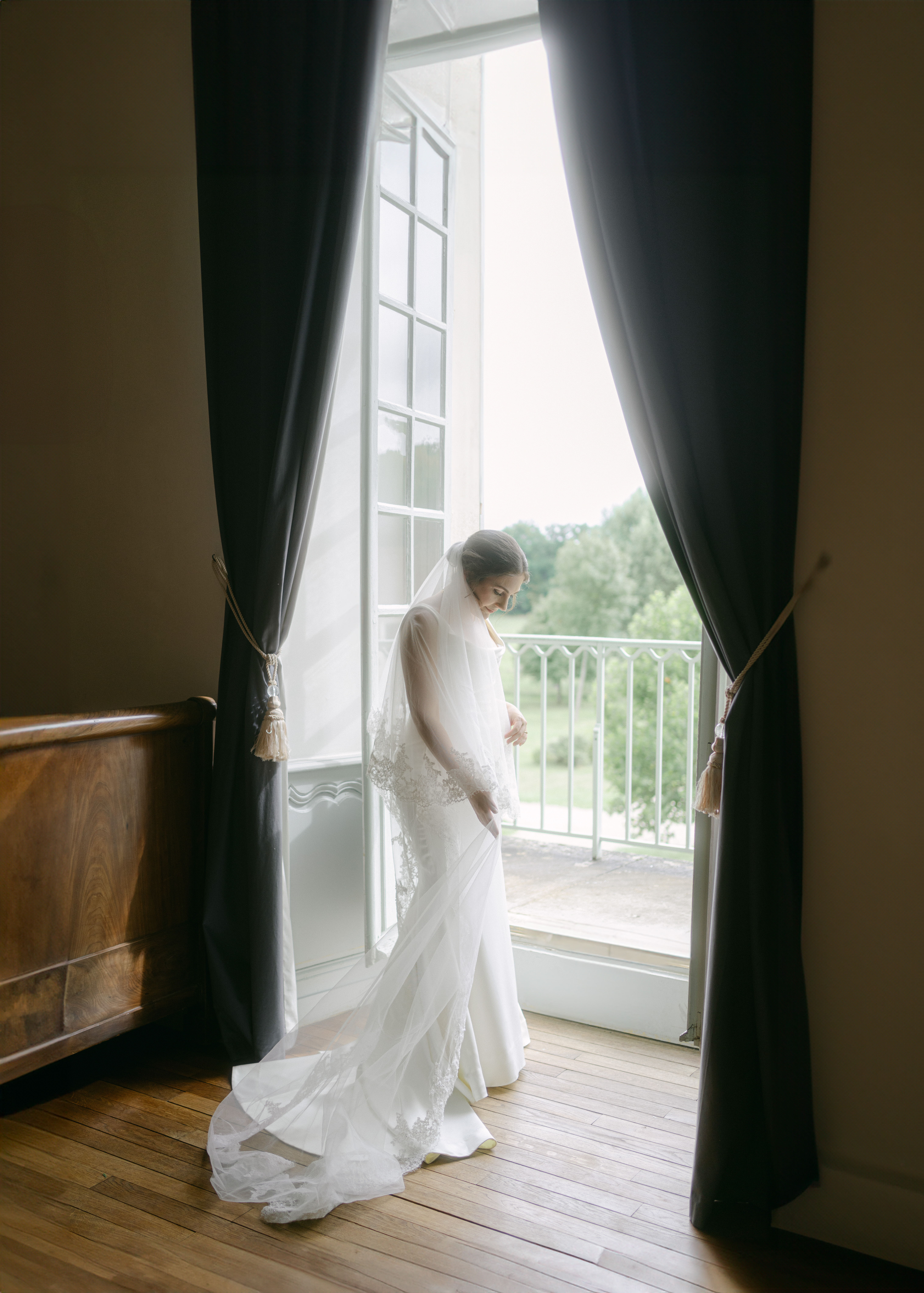 Bride stands at window on her wedding day at historic Abbaye de Reigny. Photographed by France Wedding Photographer Pia Bacino